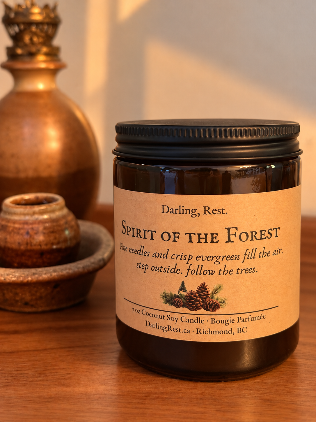 Spirit of the Forest candle in an amber glass jar on a wooden tabletop beside an antique brass oil lamp in warm golden light